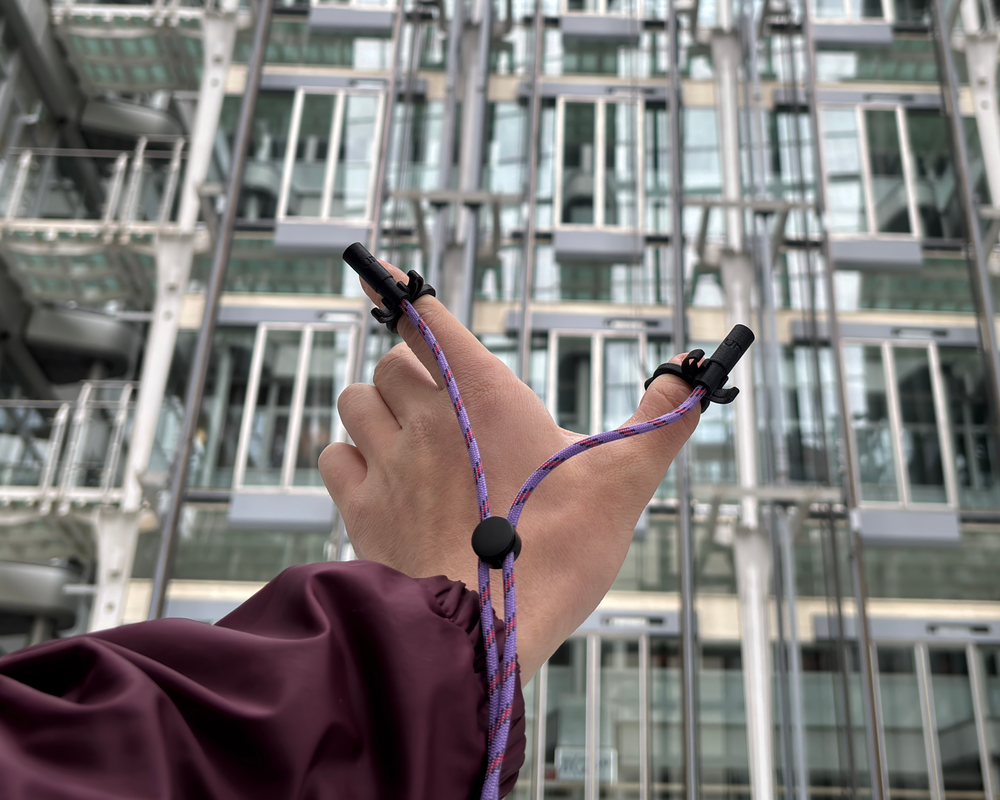 ONELAV capsules clipped to a hand's fingers on a purple braided cable, glass building behind